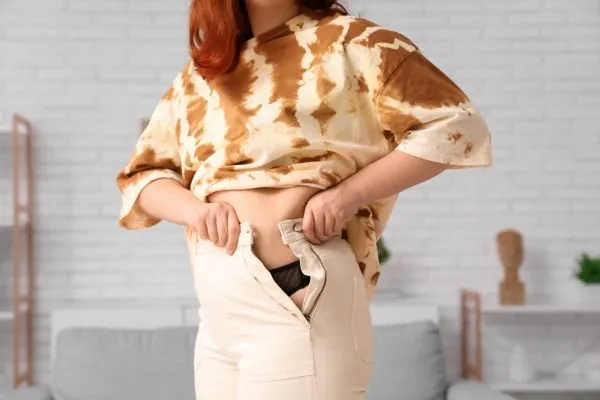 Image of woman trying to do her trousers up after pregnancy weight gain Chelmsford